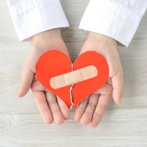 Torn heart with adhesive plaster covered by child's hands