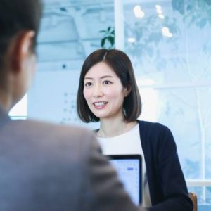 An asian business woman and a caucasian woman discussing in a conference room.  One person talking, the other listening